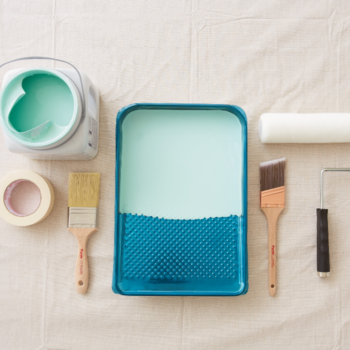 Overhead shot of a paint can, painter’s tape, paintbrushes, tray and roller on a paint tarp.